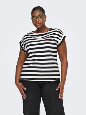 Woman wearing round glasses, black and white striped shirt, and black pants, standing with hands relaxed by sides against plain background.