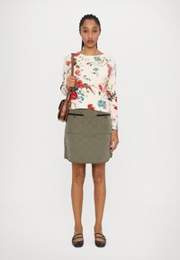 Pull en tricot à motifs floraux en crème et rouge, assorti à une jupe matelassée olive avec des poches plates et une finition lisse.
