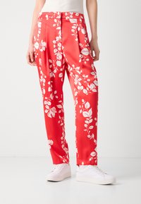 Røde bukser med blomsterdesign i glatt stoff med hvite botaniske mønstre, med folder og en avslappet passform, parret med hvite sneakers.