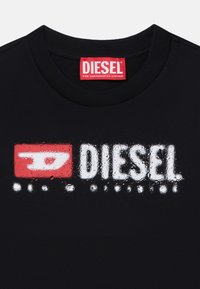 Crna pamučna majica s istaknutim bijelim i crvenim "DIESEL" logotipom s efektom trošenja i okruglim izrezom.