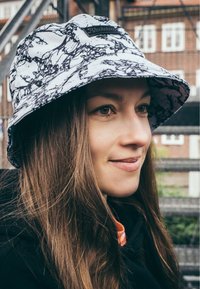 Svart och vitmönstrad bucket-hatt med bred brätte och en texturerad yta; har en liten svart etikett på framsidan.