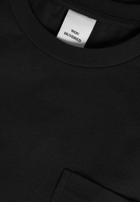 T-shirt di cotone nero con scollatura tonda e una piccola tasca. L'etichetta sulla scollatura riporta la scritta "WON HUNDRED." Texture liscia, design minimale.