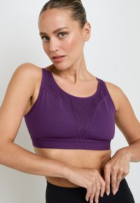 Reggiseno sportivo viola con un motivo geometrico testurizzato, spalline larghe e una fascia di supporto. Tessuto liscio con leggera lucentezza.