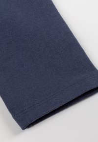 Manica in tessuto di cotone di un blu navy scuro, con una texture liscia e un orlo dritto con dettagli di cucitura visibili.