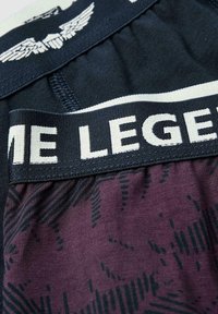 Des shorts de sport noirs et violets qui présentent une section inférieure à motifs, une taille élastique avec du texte et un emblème décoratif en haut.