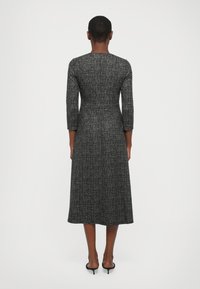 Knee-length, tettsittende svart kjole med trekvart ermer, teksturert stoff med et subtilt mønster, og rett kant.