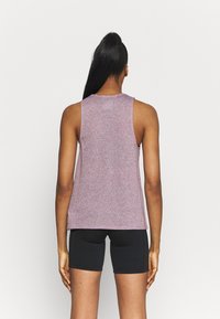 Top senza maniche in lilla heather, tessuto leggermente strutturato, scollo rotondo, orlo dritto, abbinato a pantaloni sportivi neri.