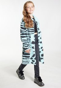 Svetlomodrý, fluffy kabát s čiernymi pruhmi a škvrnami zebry; dlhé rukávy, otvorený predok, nosený na čiernom crop tope, skombinovaný s čiernymi džínmi a topánkami.
