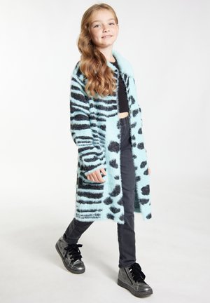 Světle modrý, načechraný kabát s černými pruhy a skvrnami zebra; dlouhé rukávy, otevřený vpředu, nošený přes černý crop top, v kombinaci s černými džíny a botami.