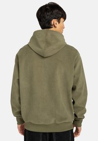 Hoodie in corda d'ulivo con cappuccio regolabile, polsini e orlo a coste; la superficie testurizzata aggiunge profondità e interesse visivo.