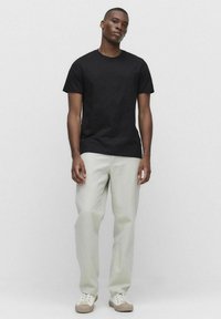 Sort kortærmet t-shirt i kombination med lysegrønne lige bukser og beige sneakers, sat mod en lys grå baggrund.