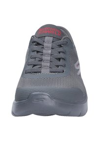 Γκρι αθλητικό παπούτσι Skechers Go Walk με επάνω μέρος από δίχτυ και κορδόνια, που φαίνεται από μπροστά, δείχνοντας το κόκκινο λογότυπο στη γλώσσα.