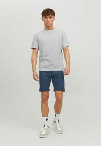 T-shirt a righe grigie e bianche, maniche corte, abbinato a pantaloni corti blu scuro. Sneakers bianche con dettagli grigi e calze bianche.