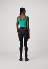 Grön ärmlös bodysuit i kombination med svarta skinny jeans, med en slät textur och klassisk femficksdesign, sedd bakifrån.