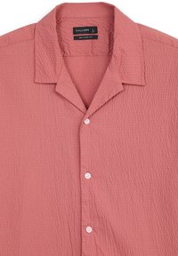 Camicia a maniche corte, dalla vestibilità rilassata, in rosa polveroso con una finitura testurizzata. Presenta un colletto a notched e bottoni bianchi. Etichetta del marchio visibile.