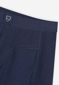 Navy blue waistband and upper section of fitted garment with visible stitching and small white leaf logo on waistband.
