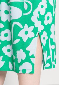 Vestido verde com um padrão floral branco, feito de tecido macio, com um detalhe de fenda lateral e um acabamento suave e uniforme.