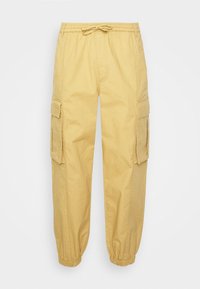 Gula cargo-byxor med elastisk midja och snörning. Har sidofickor och elastiska mudd vid anklarna. Texturerad tyg.