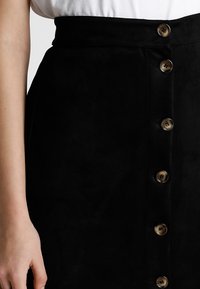 Falda de ante negra con cintura alta y cierre frontal de botones. Presenta botones en tono marrón y una textura suave, destacando un diseño minimalista.