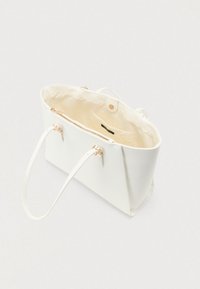 Sac fourre-tout en cuir blanc avec double poignée, doublure intérieure crème, poche intérieure et fermeture à pression magnétique, vu de dessus.