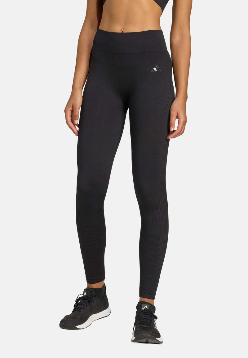 Leggings noirs taille haute en tissu extensible, avec des détails côtelés au niveau des jambes inférieures et un petit logo sur la hanche.