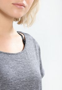 Camiseta gris de manga corta y cuello redondo con un acabado texturizado. Se puede ver una tira negra de una prenda interior debajo del cuello.