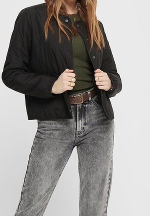 Sort quiltet jakke med trykknapper, båret over en grøn ribbet top. Grå højtaljede jeans med en let syrevaskeeffekt og et brunt bælte.
