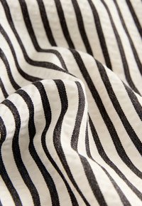 Baumwollstoff mit abwechselnden schwarzen und weißen wellenförmigen Streifen. Die Textur wirkt weich und glatt, mit einem dezenten Glanz.