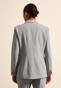 Grijze op maat gemaakte blazer met een gepolariseerde kraag, gestructureerde schoudernaden en zijventilatie, gemaakt van een gladde stof met een subtiele textuur.