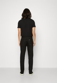 Chemise noire à manches courtes associée à un pantalon noir. La tenue présente un design simple, avec un look épuré et une coupe standard.