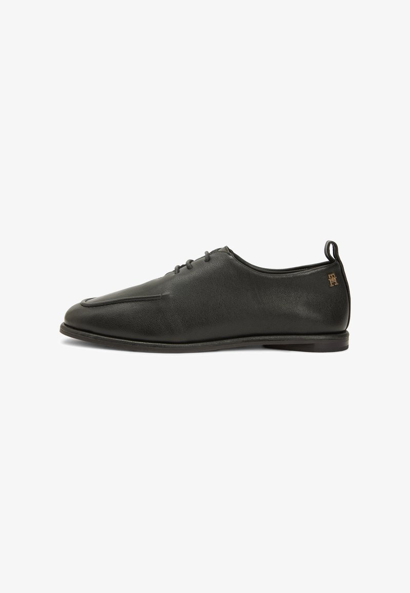 Chaussure habillée pour homme en cuir noir à profil bas avec fermeture à lacets à l'avant et logo embossé discret près du talon, sur fond blanc.