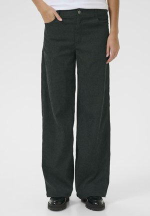 Pantalons larges vert foncé en tissu texturé, dotés de poches latérales et d'une fermeture à bouton à l'avant. Associés à des chaussures noires.