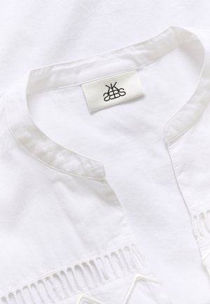 White cotton shirt with a mandarin collar, featuring intricate embroidery and cutout details along the chest. Label is visible.