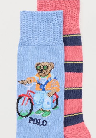 Ζευγάρι κάλτσες, η μία γαλάζια με μια αρκούδα σε κόκκινο ποδήλατο που φοράει γυαλιά ηλίου και ρούχα, η άλλη ροζ με ναυτικό μπλε και κίτρινες ρίγες.