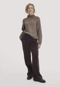 Bruine gebreide trui met een hoge kraag, gecombineerd met donkerpaarse corduroy flared pants. De outfit heeft ribgebreide boorden en een relaxed fit.