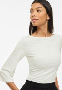 Balts, garām piedurknēm tops ar laivas kakla izgriezumu, pieguļošu piegriezumu un mīkstu tekstūru, kombinēts ar augsta vidukļa melnām biksēm.