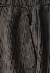 Mörkgrått texturerat tyg med vertikala veck och midjeband i elastiskt material. Tyget verkar mjukt och lättviktigt.