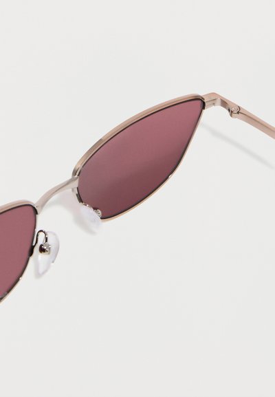 Ochelari de soare cu ramă metalică, lentile în formă de ochi de pisică de culoare roz închis și pernuțe nazale reglabile, transparente, pe un fundal alb.