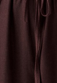 Burgundiškos fliso sportinės kelnės su minkšta tekstūra, elastinga juosmens juosta ir raišteliu užsegimui. Yra siūtos siūlės, skirtos patvarumui.