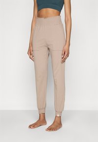 Jogging beige a gamba affusolata realizzati in tessuto morbido, con una vita smock elasticizzata e due tasche frontali.