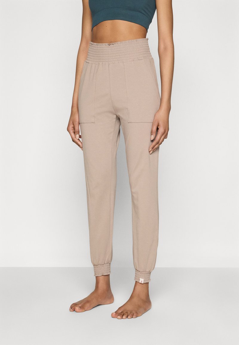 Jogging beige a gamba affusolata realizzati in tessuto morbido, con una vita smock elasticizzata e due tasche frontali.