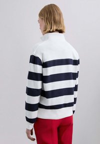 Jersey de rayas blancas y azul marino con cuello alto y mangas largas, de corte holgado, combinado con pantalones rojos.
