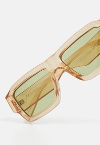 Glasses with a transparent amber acetate frame and rectangular green-tinted lenses, featuring minimalist accents and a sturdy design.