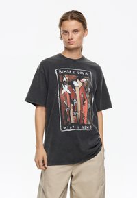 Camiseta de algodón negra de gran tamaño con un diseño gráfico audaz y colorido que presenta elementos florales abstractos y el nombre de la marca "Bimbay Lola."