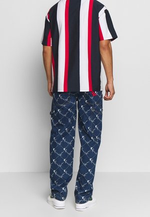 Camisa de manga corta a rayas en azul marino, blanco y rojo, combinada con pantalones cargo azules con un patrón floral blanco y múltiples bolsillos.
