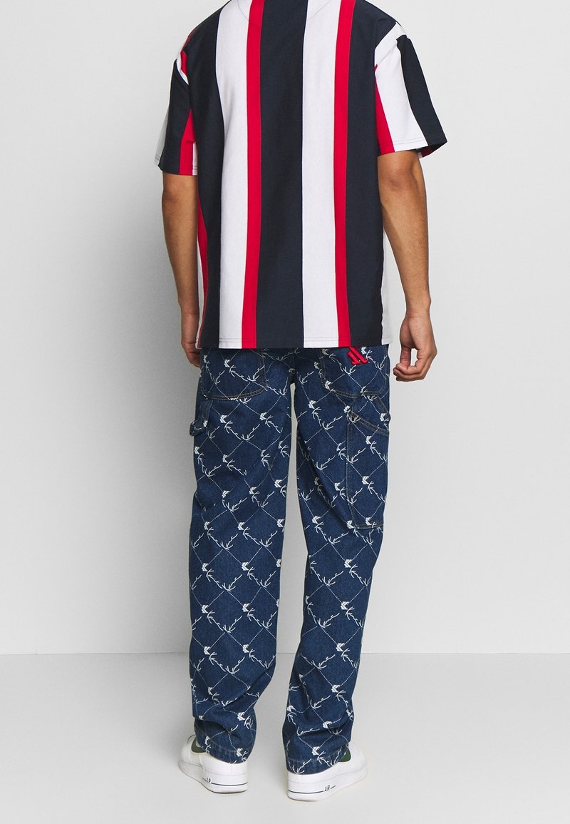 Pruhovaná košile s krátkým rukávem v námořnické modré, b ílé a červené barvě, spárovaná s modrými cargo kalhotami s bílým květinovým vzorem a několika kapsami.