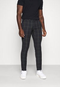 Skurna rutiga byxor i mörka nyanser, med smal passform, rutig mönster och en mjuk tygkvalitet, parat med vita sneakers.