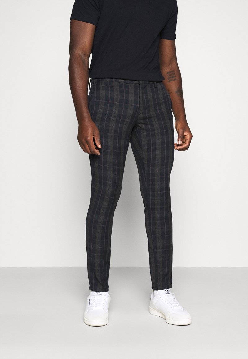 Skurna rutiga byxor i mörka nyanser, med smal passform, rutig mönster och en mjuk tygkvalitet, parat med vita sneakers.