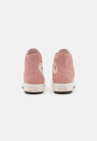 Zapatillas altas de lona rosa con suelas y costuras de goma blanca, que cuentan con un parche de logo en cada talón y puntas redondeadas.