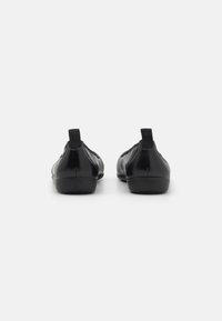 Des chaussures noires à enfiler avec une texture en cuir lisse, un bout rond et une languette au dos. Conçues avec une semelle profilée basse pour le confort.